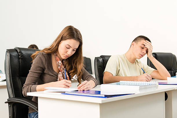 estudantes do ensino médio escrevendo na mesa da sala de aula - schoolgirl boredom frustration adult student - fotografias e filmes do acervo