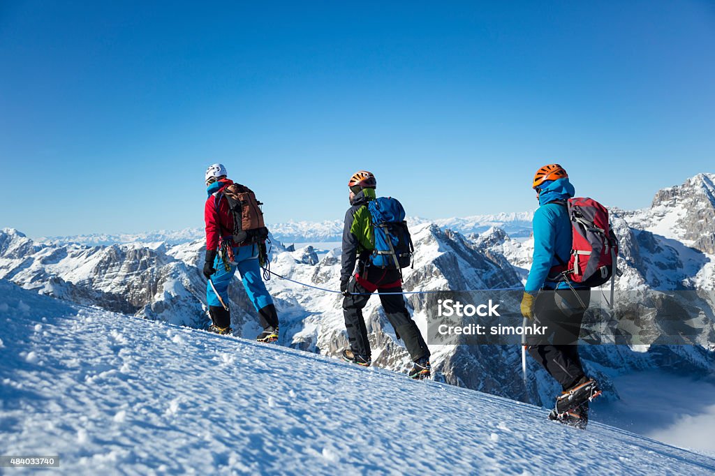 Men hiking on snow covered landscape Julian Alps, Triglav National Park, Three hikers carrying backpacks and climbing rope moving up on snow covered mountain, mountain peaks in background. Snow Stock Photo