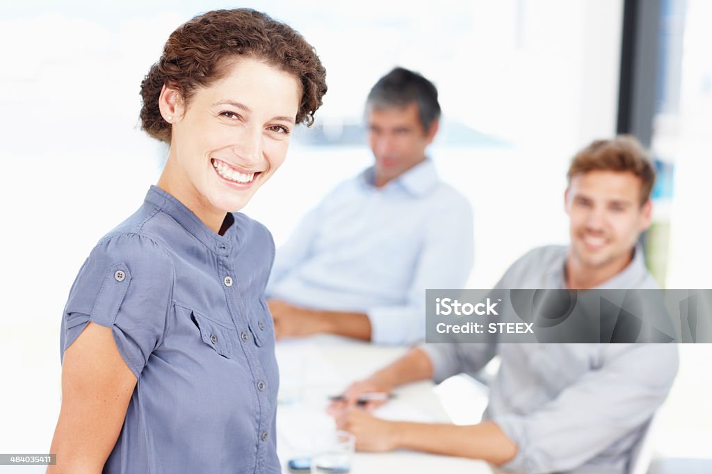 Taking on the business world with a smile Portrait of a smiling office worker with colleagues sitting behind her 20-29 Years Stock Photo