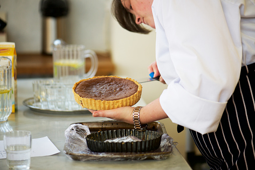 woman chef in profile stooped check carefully and Use an offset spatula to release  the crust from the bottom of the tart pan