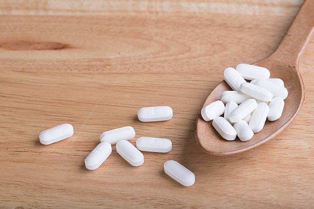 istock White pill on wood spoon and wood table 484044670