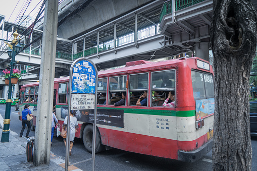 Bangkok, Thailand - August 6, 2015:  Commuters are boarding the Red Bus from an obsolete Bangkok Bus Stop.