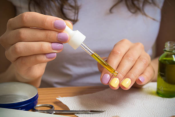 Female hand holding a pipette with oil Female hand holding a pipette with oil. A young girl sits at a table and gets a yellow oil on the nails. On the table are nail clippers, a bottle of oil, a jar of cream and other nail accessories. cuticle photos stock pictures, royalty-free photos & images