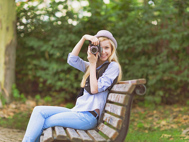 istock Young hipster taking photo sitting on bench in the park 484063743