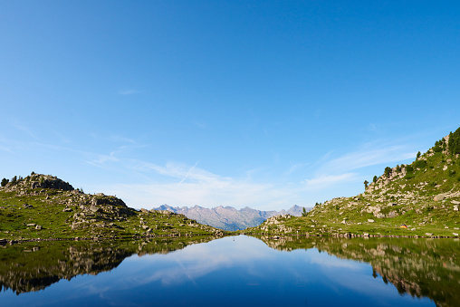 Scenic landscape with turquoise mountain lake in autumn valley against large snow mountains in low clouds in morning sunlight. Alpine lake with view to sunlit high snowy mountain range in low clouds.