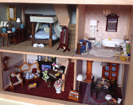 Photo showing the front of an opened wooden dolls house, with lounge and dining room, bedroom, bathroom, stairs, carpet, wallpaper and miniature furniture.