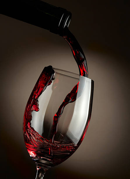 Red wine pouring in glass over dark background stock photo