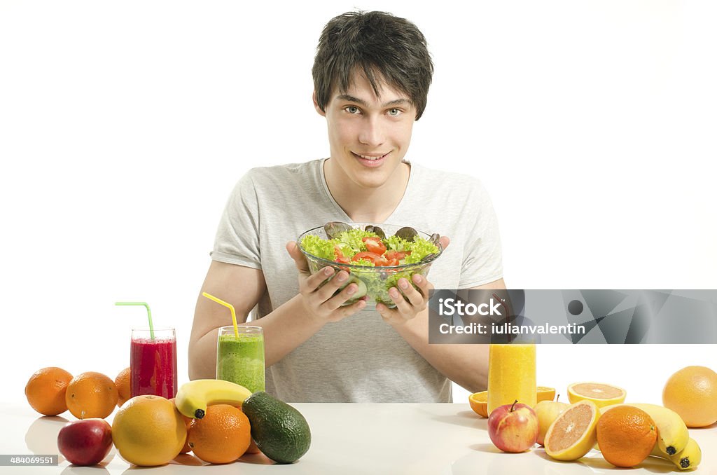 Man having a table withorganic food,juices, smoothie,salad Happy man having a table full of organic food,juices and smoothie. Cheerful young man eating healthy salad and fruits. Isolated on white. Adult Stock Photo