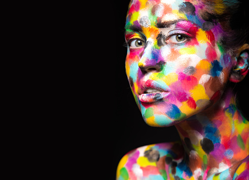 Girl with colored face painted. Art beauty image. Picture taken in the studio on a black background.