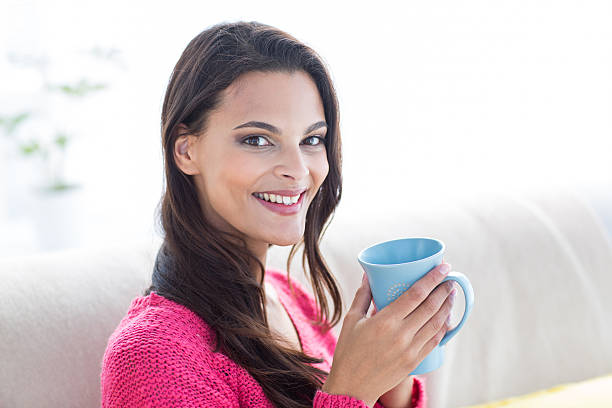 istock Smiling beautiful brunette relaxing on the couch and holding mug 484091998