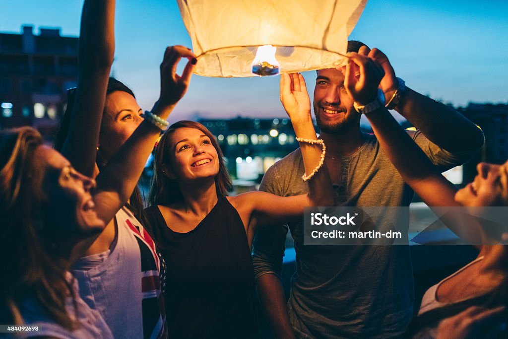 Friends releasing paper lantern for New Year Happy friends on a rooftop party holding a sky lantern New Year Stock Photo