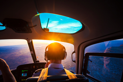 Helicopter pilot flying a helicopter over the Las Vegas desert during sunset. A sun flare can be seen entering the cockpit.
