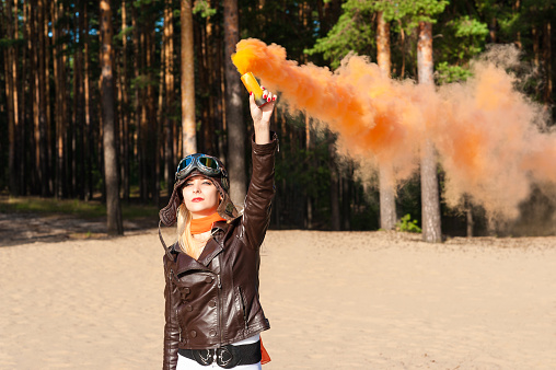 beautiful woman dressed as a pilot standing on the shore of the beach with a colored smoke bombs