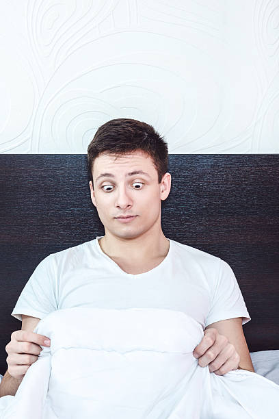 good young man in bed looking down at his penis stock photo