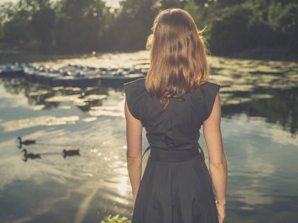 istock Young woman standing by lake at sunset 484122256