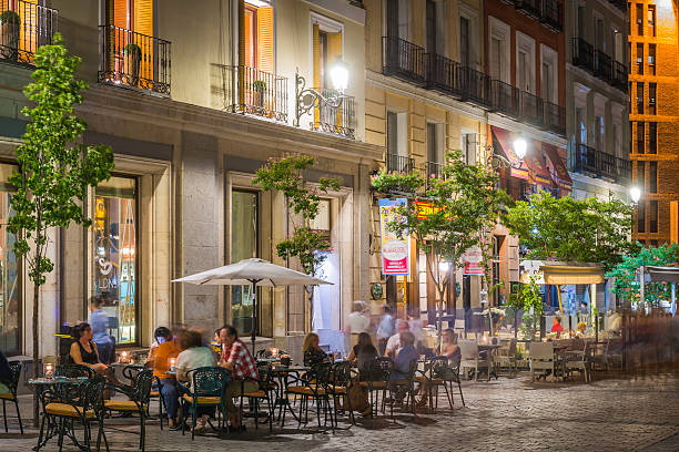 Madrid, Spain - July 12, 2015: People relaxing at the al fresco tables of the pavement restaurant bars illuminated by warm lamp light in historic central Madrid, Spain's vibrant capital city. 
