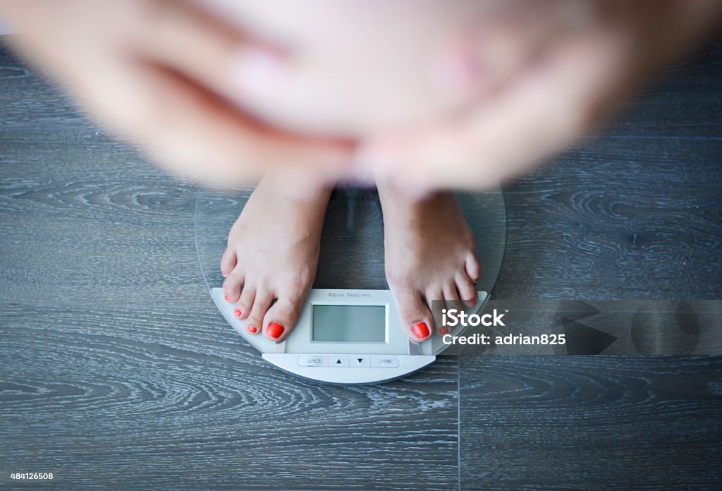 Pregnant woman weighing herself on a bathroom scale Mass - Unit of Measurement Stock Photo