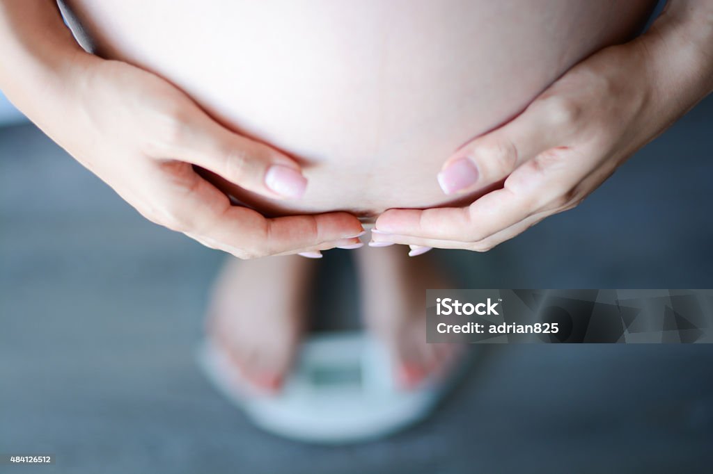 Pregnant woman weighing herself on a bathroom scale Pregnant Stock Photo