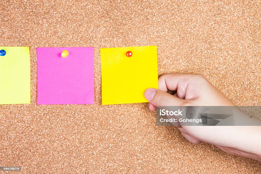 multicolor reminder sticky notes on cork board with hand holding - Royaltyfri Kork - Material Bildbanksbilder