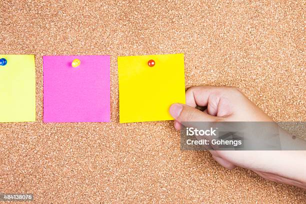 Multicolor Reminder Sticky Notes On Cork Board With Hand Holding-foton och fler bilder på Kork - Material