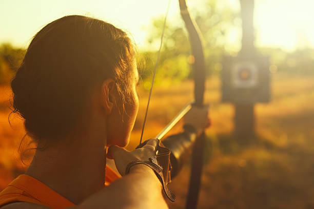 feminino archer no campo ao pôr-do-sol - archery bow arrow women - fotografias e filmes do acervo