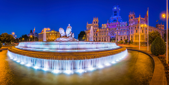 Spotlights illuminating the 18th Century fountain of Cybele overlooked by the iconic towers of the Palacio de Cibeles colourfully lit against the deep blue dusk skies above the Plaza de Cibeles in the heart of downtown Madrid, Spain's vibrant capital city. ProPhoto RGB profile for maximum color fidelity and gamut.