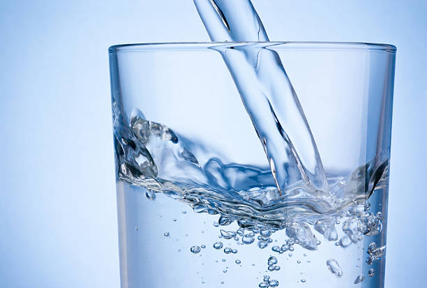 nahaufnahme gießen wasser in ein glas auf blauem hintergrund - gurgling stock-fotos und bilder