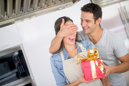 Romantic man surprising woman with a present at home and covering her eyes