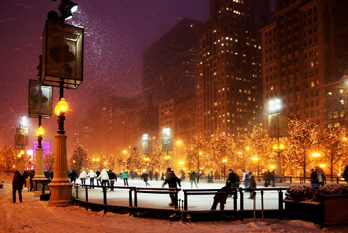 People having fun ice skating at ice rink in downtown Chicago. Beautiful snowstorm night and South Michigan Avenue lights.