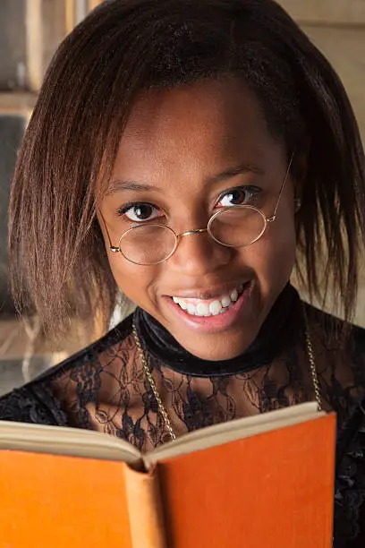 Cute black student reading a book. she is wearing a Victorian-style dress and period spectacles.