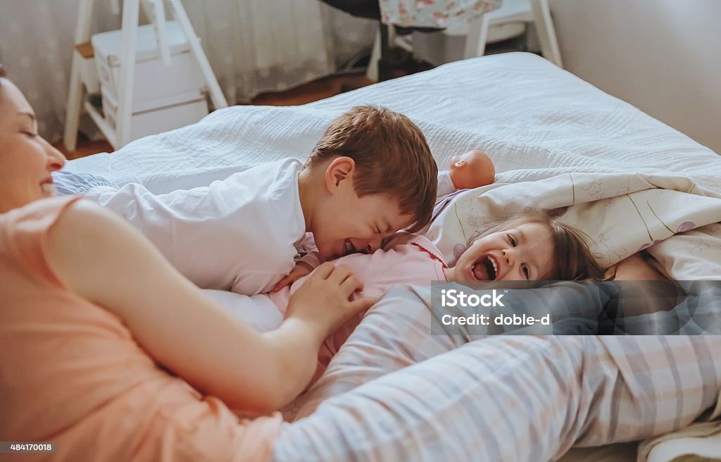 Relaxed mother and sons playing over the bed Closeup of happy family playing over the bed in a relaxed morning. Weekend family leisure time concept. 2015 Stock Photo