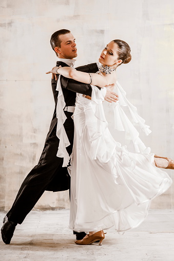 couple of young people, a girl and a young man dancing ballroom dancing in the studio, a young woman dressed in a beautiful white dress, a man in a frock coat, they are positive and happy, proffesionaly champions dance, quickstep, slow waltz, tango, slow foxtrot, Viennese Waltz