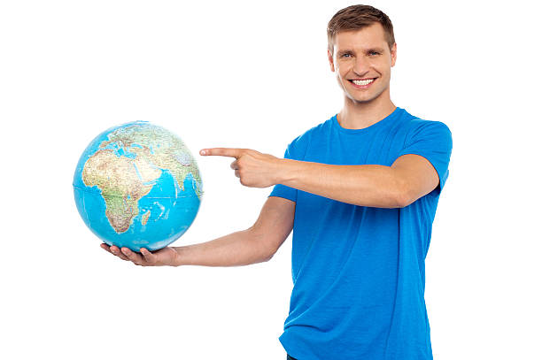 Handsome young caucasian pointing at globe Handsome young smiling caucasian holding and pointing at the globe finger spinning globe stock pictures, royalty-free photos & images
