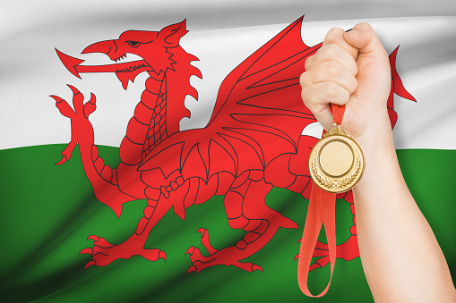 Sportsman holding gold medal with flag on background - Wales