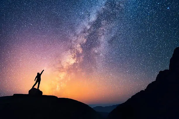 A person is standing next to the Milky Way galaxy pointing on a bright star.