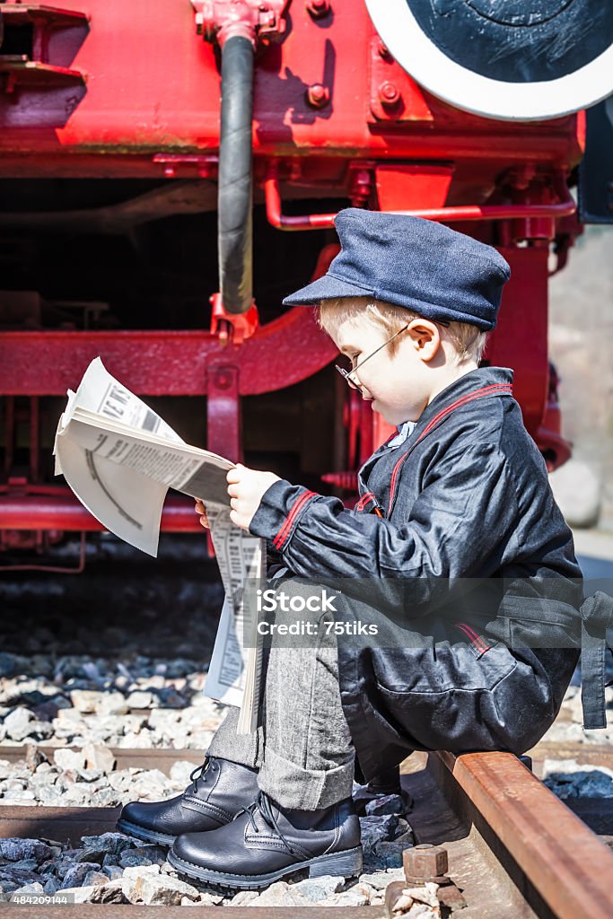 Newspaper Break Small child boy as nostalgic locomotive driver sitting at the railway track and reading a newspaper at lunch hour 2015 Stock Photo