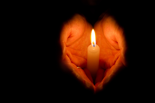 Religious concept. Man hands holding a burning candle on dark background