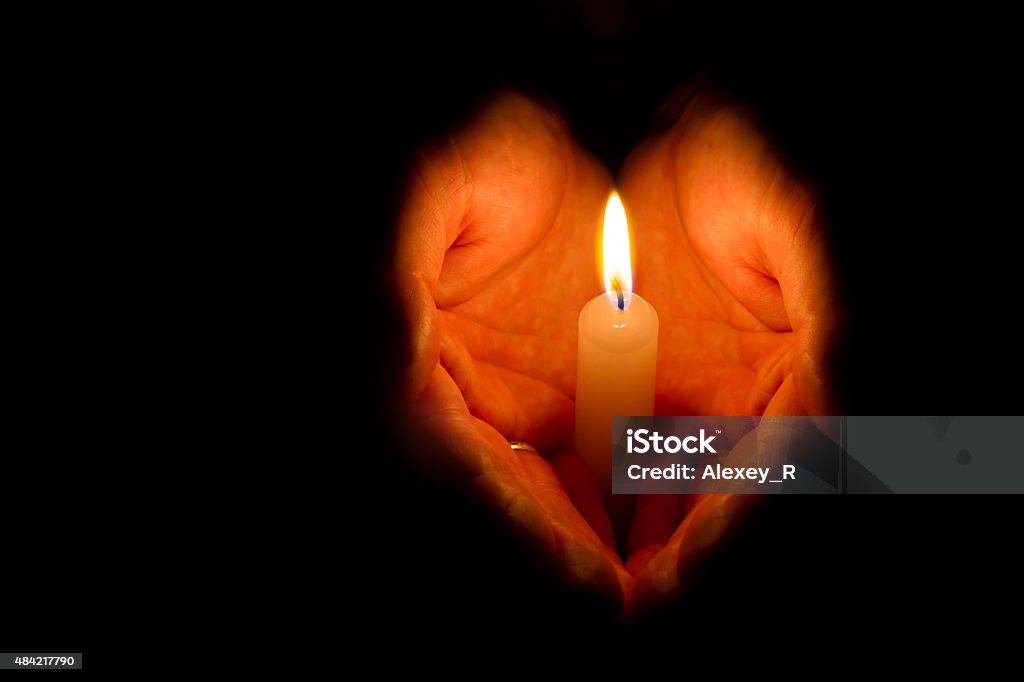 Man hands holding a burning candle Religious concept. Man hands holding a burning candle on dark background Candle Stock Photo