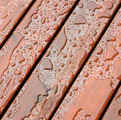 Square format close-up of stained and protected wooden decking following heavy rain.
