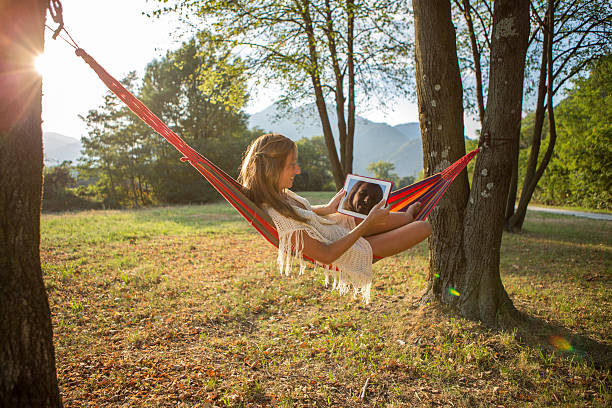 istock Young woman relaxing on hammock using digital tablet-Sunset 484218272