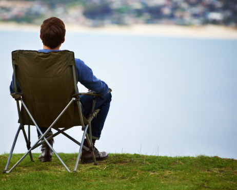 Rear-view of a young man sitting on a camping chair and looking at the view
