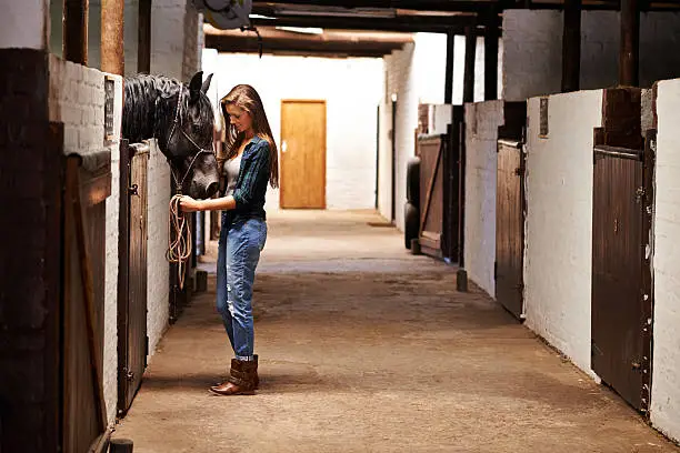 Full length shot of a young woman in a stable with her horse
