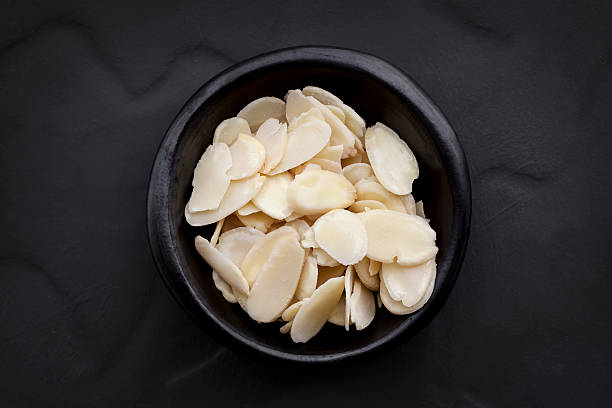 Almond Flakes in Black Bowl over Dark Slate Overhead View. Almond flakes in small black bowl over dark slate.  Overhead view. almond slivers stock pictures, royalty-free photos & images