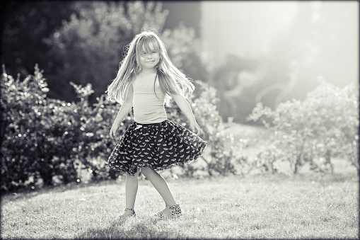 Cute little girl with skirt, dancing and swirling around, summertime outdoors