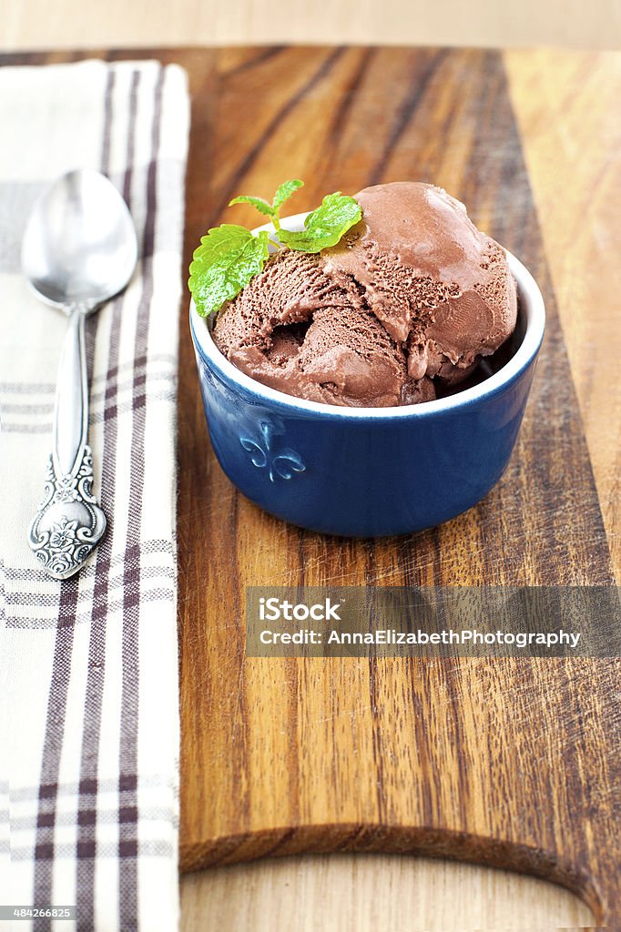 Chocolate ice-cream in porcelain bowl. Closeup. Chocolate ice-cream with green mint leaf in blue porcelain bowl on wooden cutting board. Closeup. Bowl Stock Photo