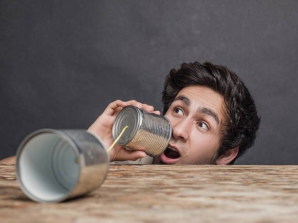 Portrait of young man using tin can phone. Horizontal composition. Image taken in studio with Hasselblad H5D and developed from Raw.