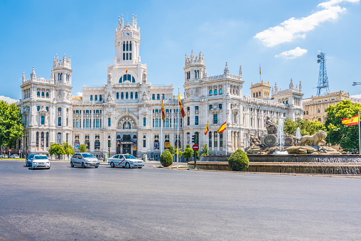 Madrid, Spain - July 19, 2022: Plaza de Cibeles. A busy city street with traffic lights. White buildings resembling castles are alongside the road.