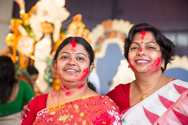 Married Bengali Hindu women from India play and smear vermilion on each other during Sindur Khela, a traditional ceremony on the final day of Durga Puja festival. Two women pose for the camera after having played.