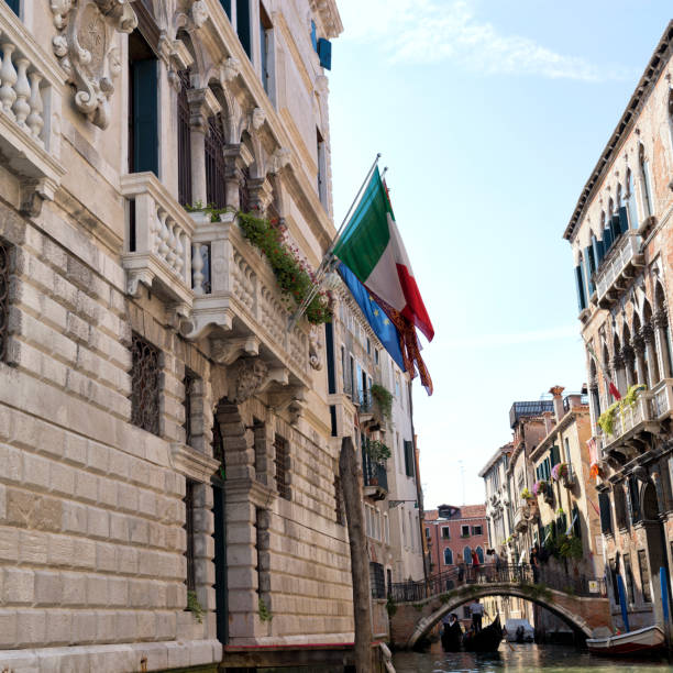 Venice, Italy - July 31, 2015: People stand on the bridge while a gondola passing by the canal during a hot summer day.
