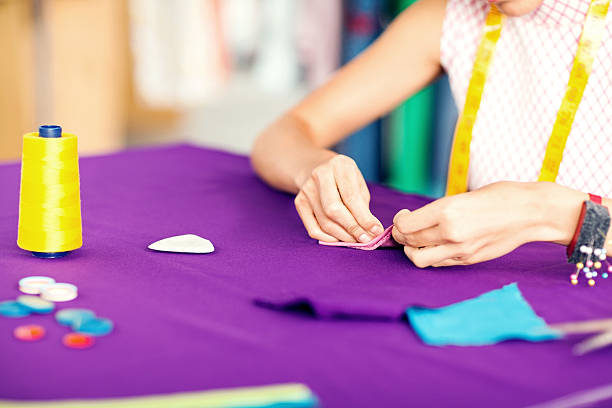 Midsection of female designer sewing textile in fashion studio. Horizontal shot.